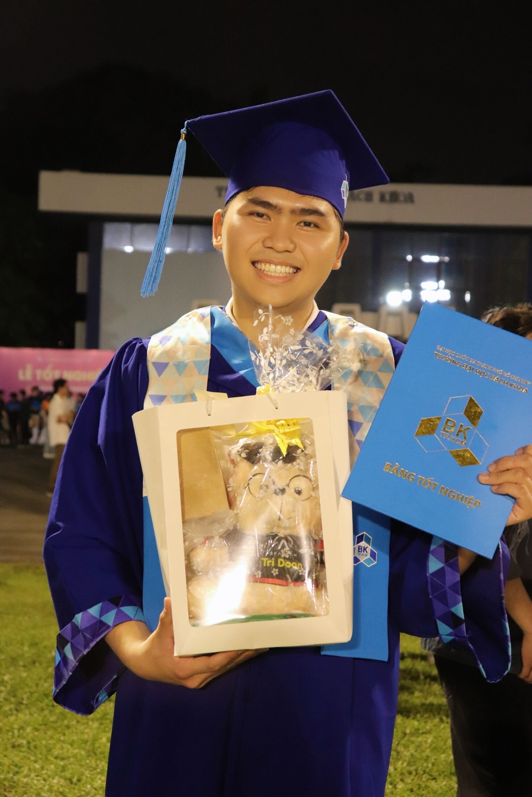 Tri smiling in his graduation gown while holding his HCMUT degree